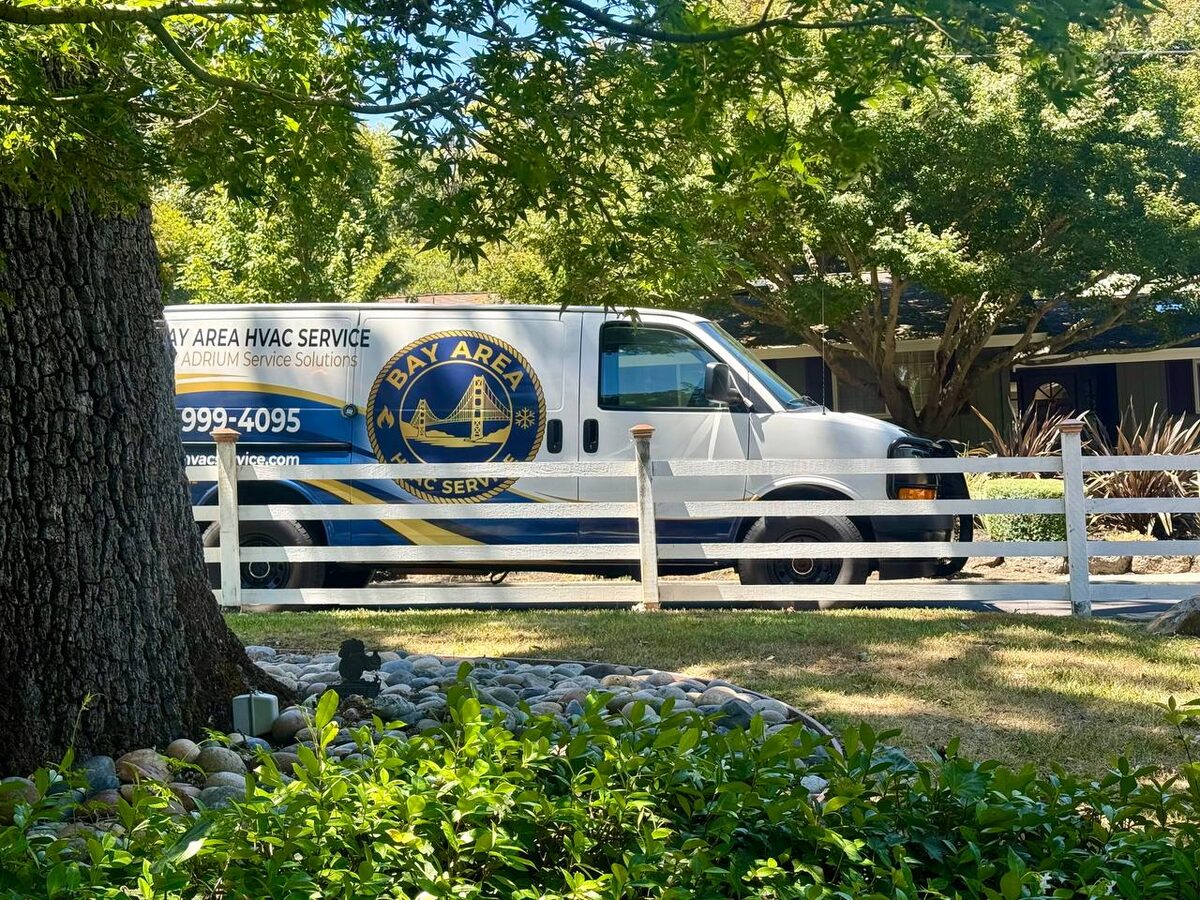 Bay Area HVAC Service van parked behind a white fence and trees
