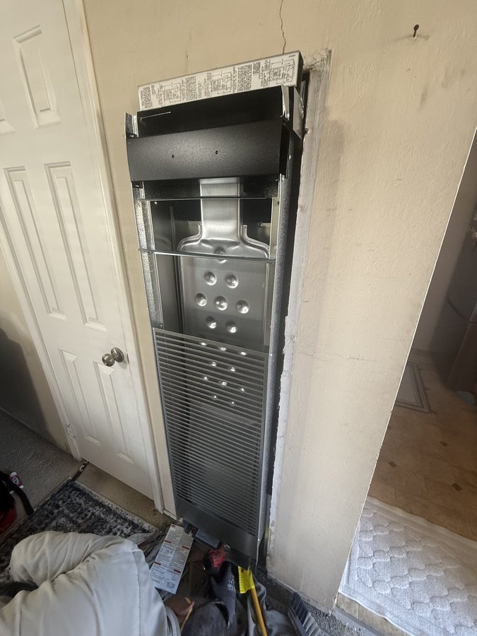 Wall furnace body set into the stud bay with front cover off, internal heat exchanger exposed during installation, Newark