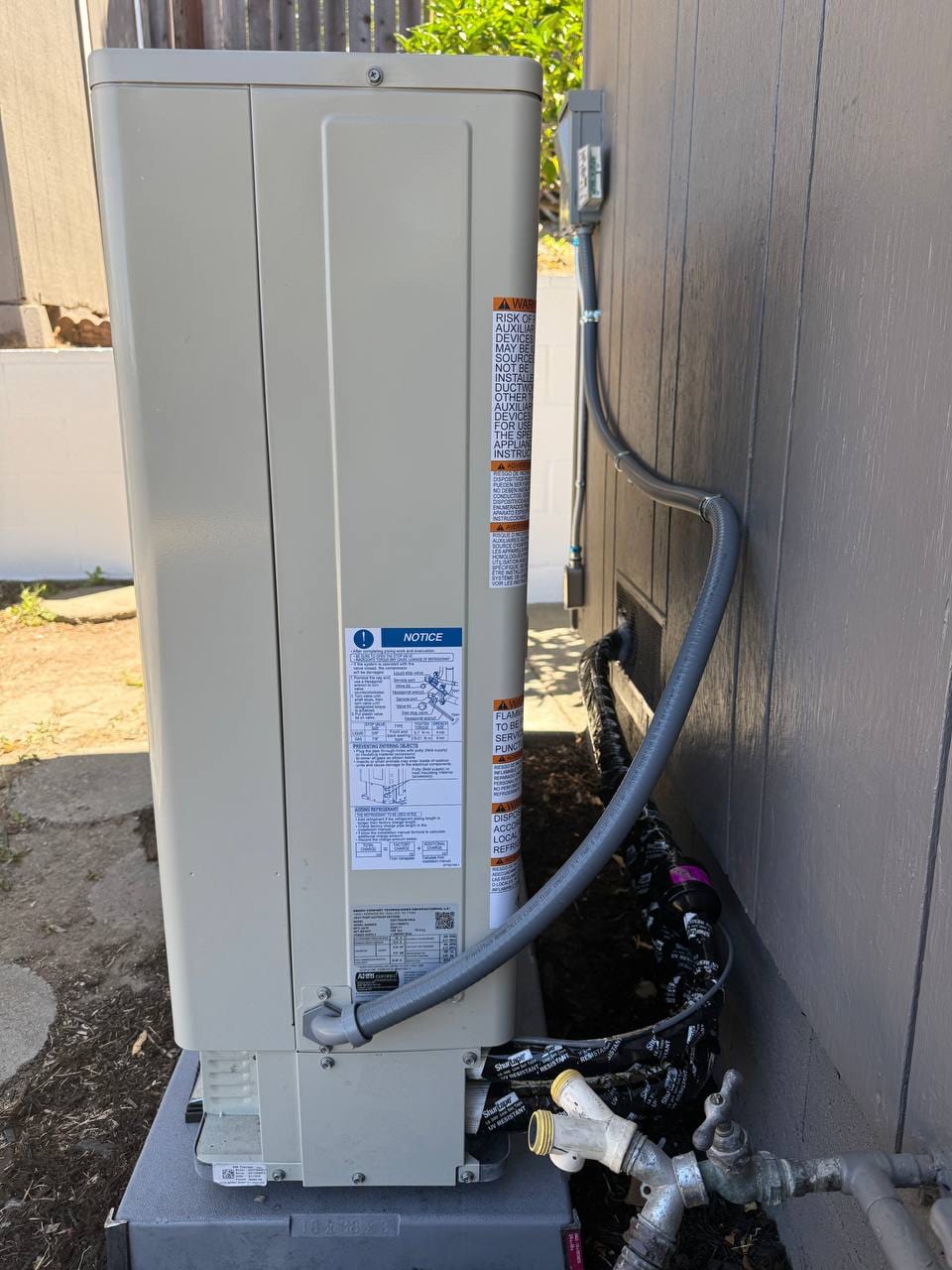 New Goodman heat pump condenser installed on pad with disconnect and line-set covers, Martinez