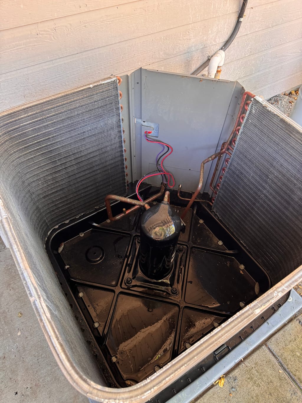 Rinsed cabinet base and exposed coil fins around the compressor after cleaning in Clayton