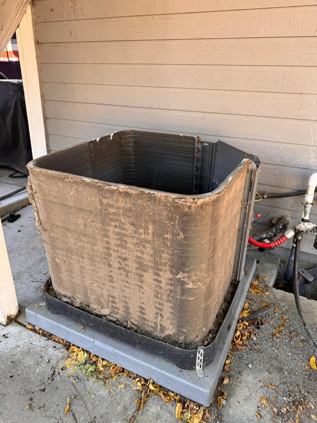 Dust and lint covering the Rheem outdoor coil beside the beige wall before cleaning in Clayton